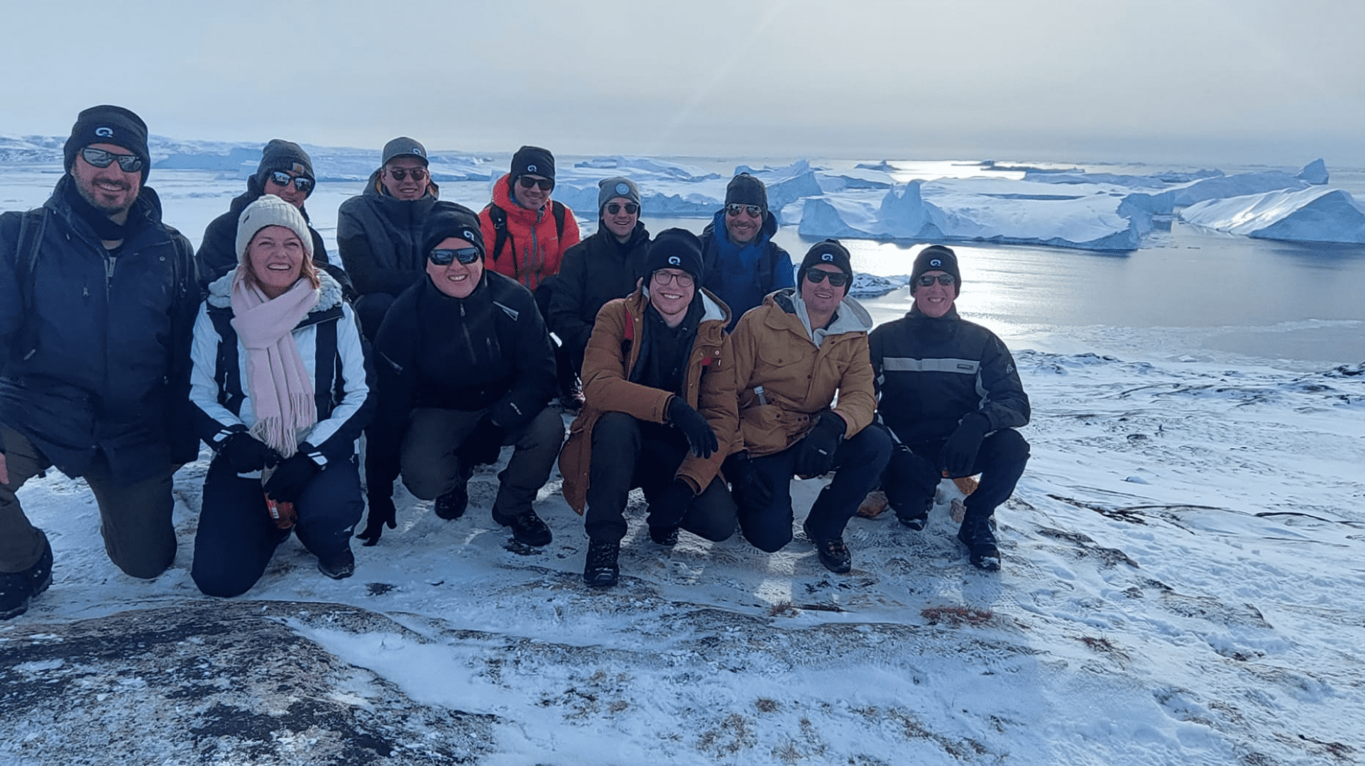 Group of people from the QCIFY team squatting down for group photo in arctic with snow and water