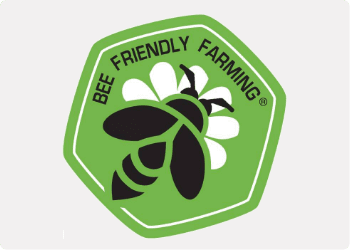 Green badge of Bee Friendly Farming with black outline of bee on white daisy petals logo